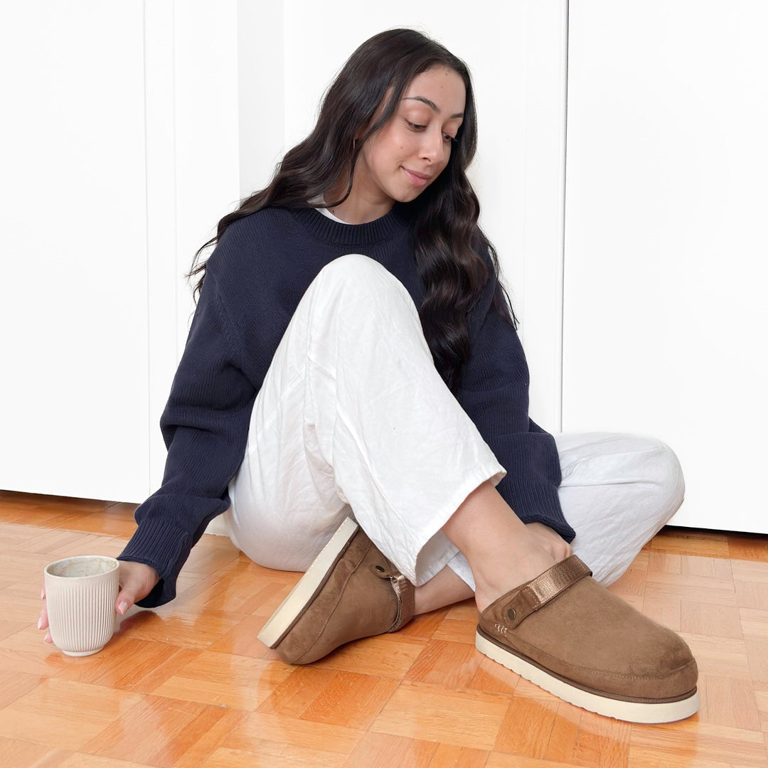 Woman sitting on a wooden floor wearing brown platform clogs