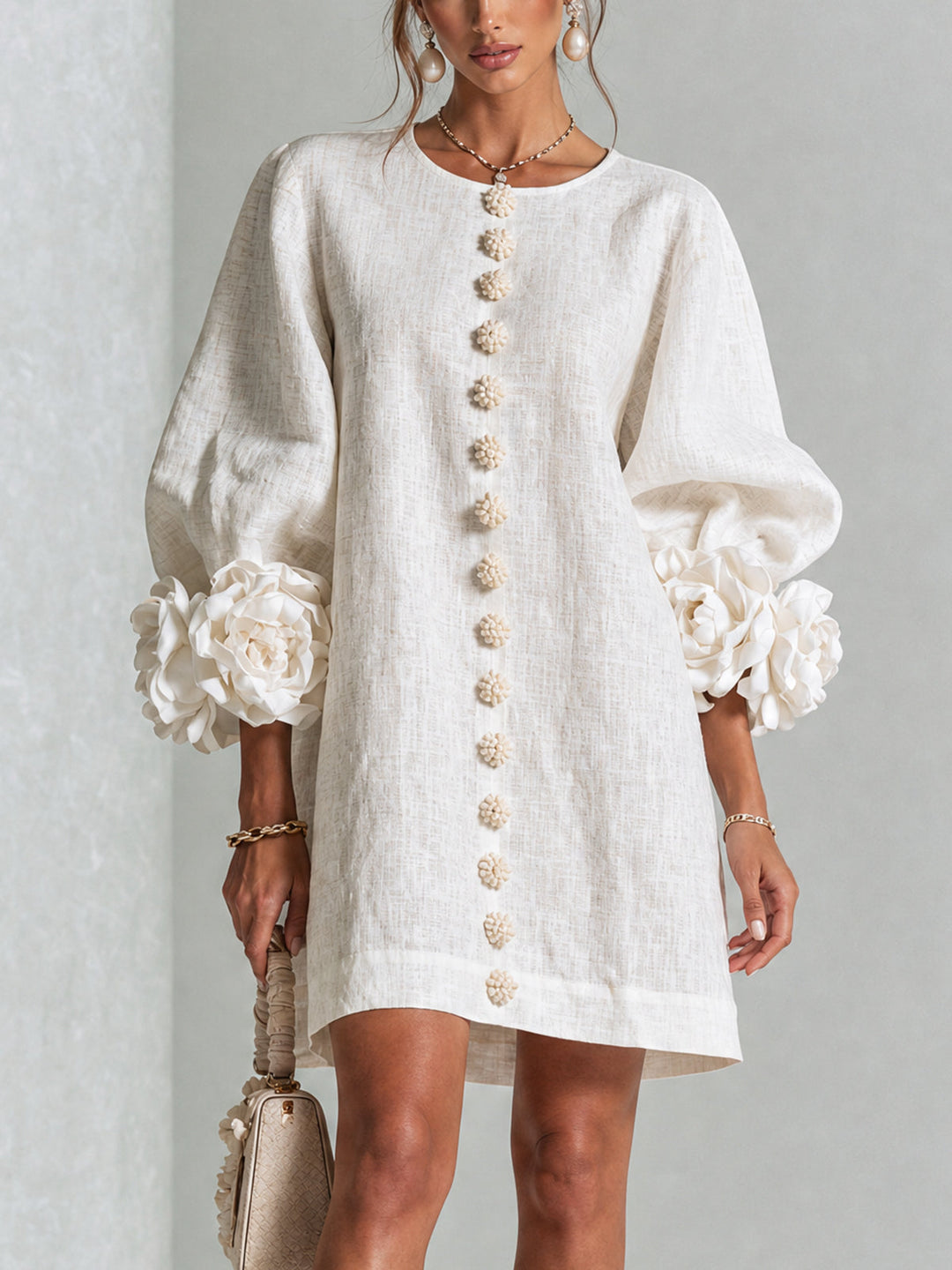 Close-up front view of a woman wearing a white puff-sleeve mini shift dress with decorative floral cuffs and buttons.