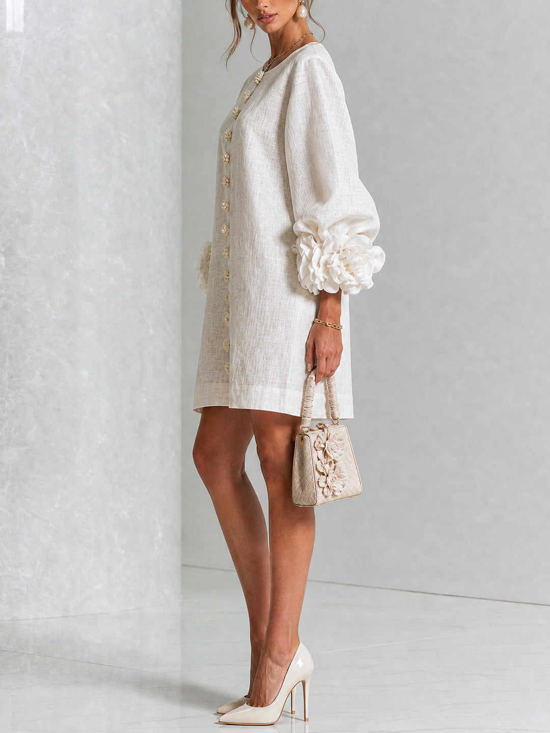 Side profile view of a woman wearing a white button-front shift dress paired with heels and a small handbag.