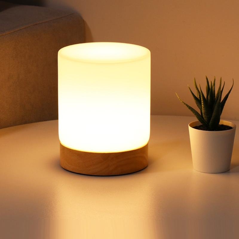 Modern glass touch LED table lamp glowing softly on a white surface next to a small potted plant