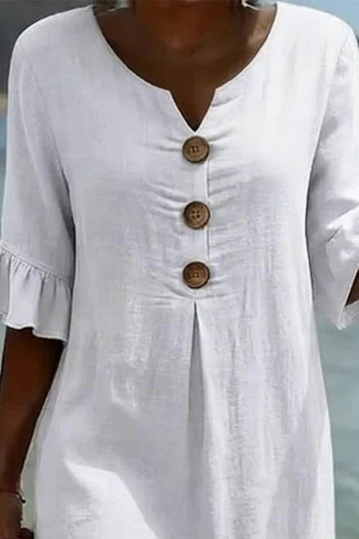 Detailed view of the V-neckline and button detailing on the white dress