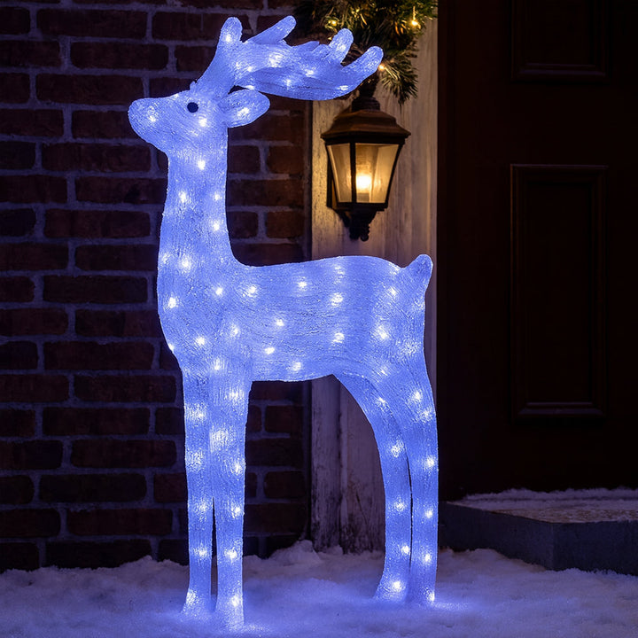 Outdoor holiday display of a lit acrylic reindeer standing on snow by a doorway