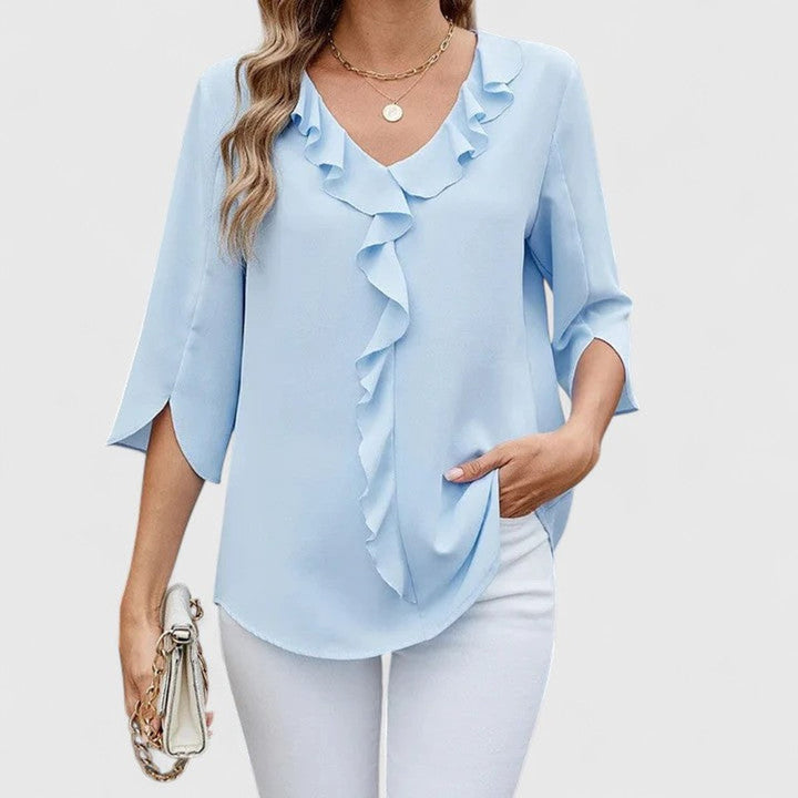Woman wearing a light blue ruffle front V-neck 3/4 sleeve blouse paired with white trousers