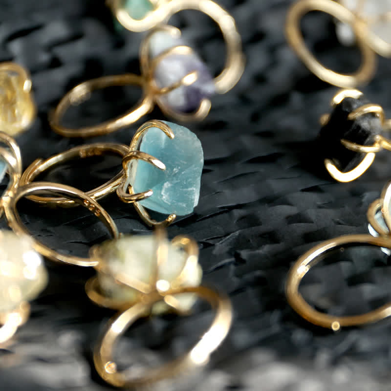 Close-up of multiple adjustable crystal rings with raw stones in gold and silver finishes