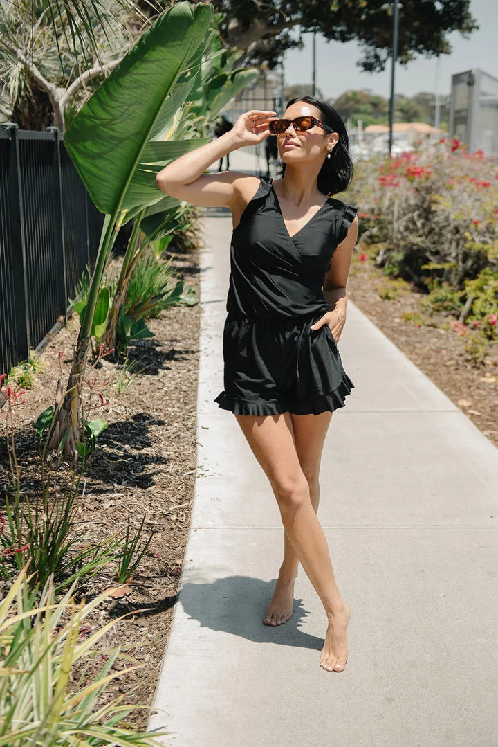 Full-body shot of a woman wearing black Aisling swimwear near tropical plants