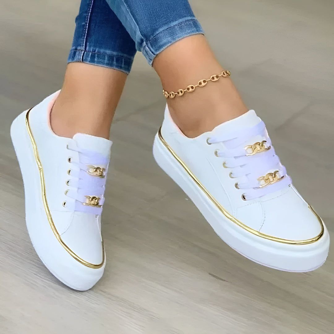 White women's lace-up flatform sneakers with gold chain detail worn with blue jeans