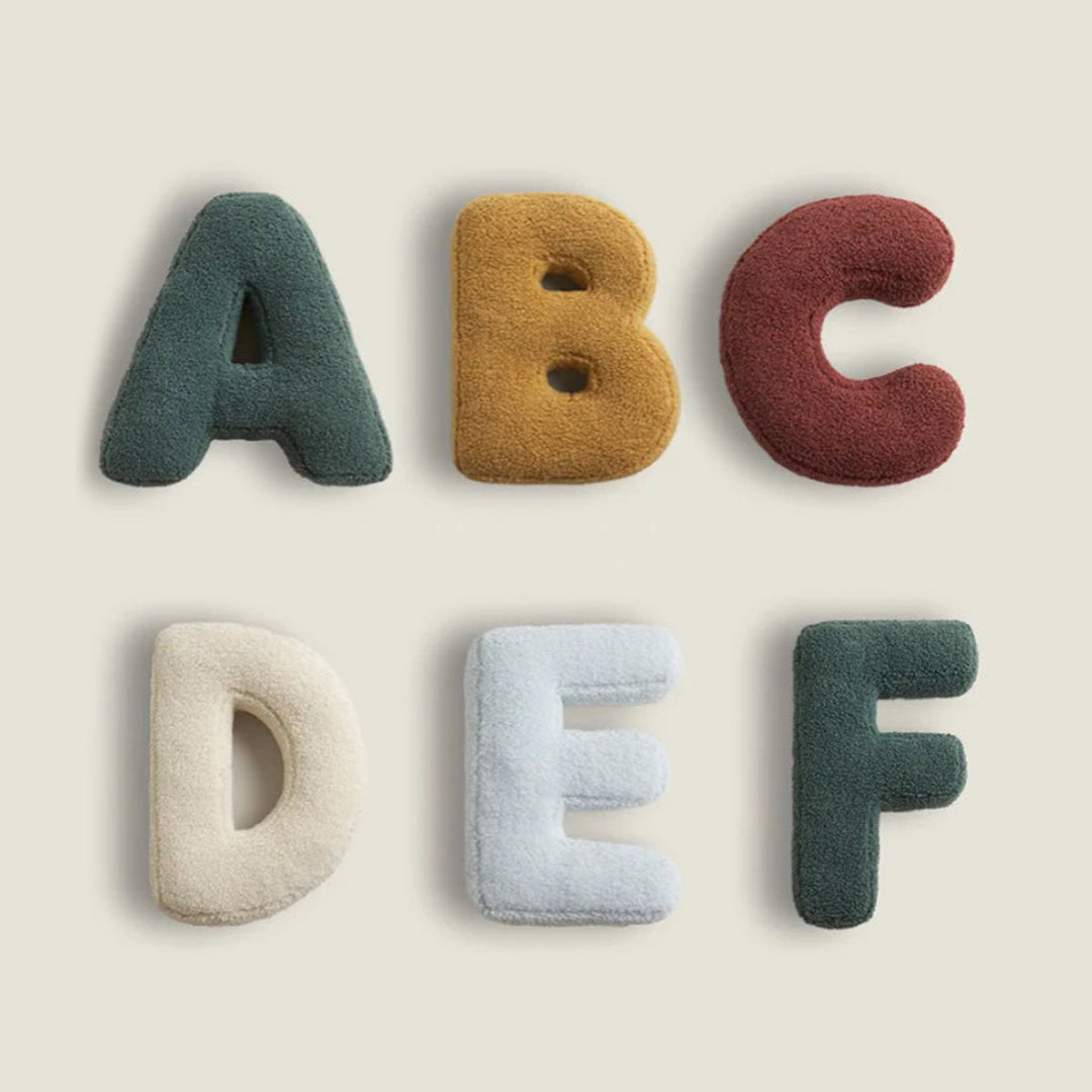 Assorted colorful alphabet decorative cushions displayed together on a neutral background