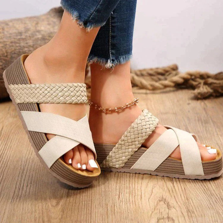 Close-up of a woman wearing beige platform slip-on sandals with a woven crossover design
