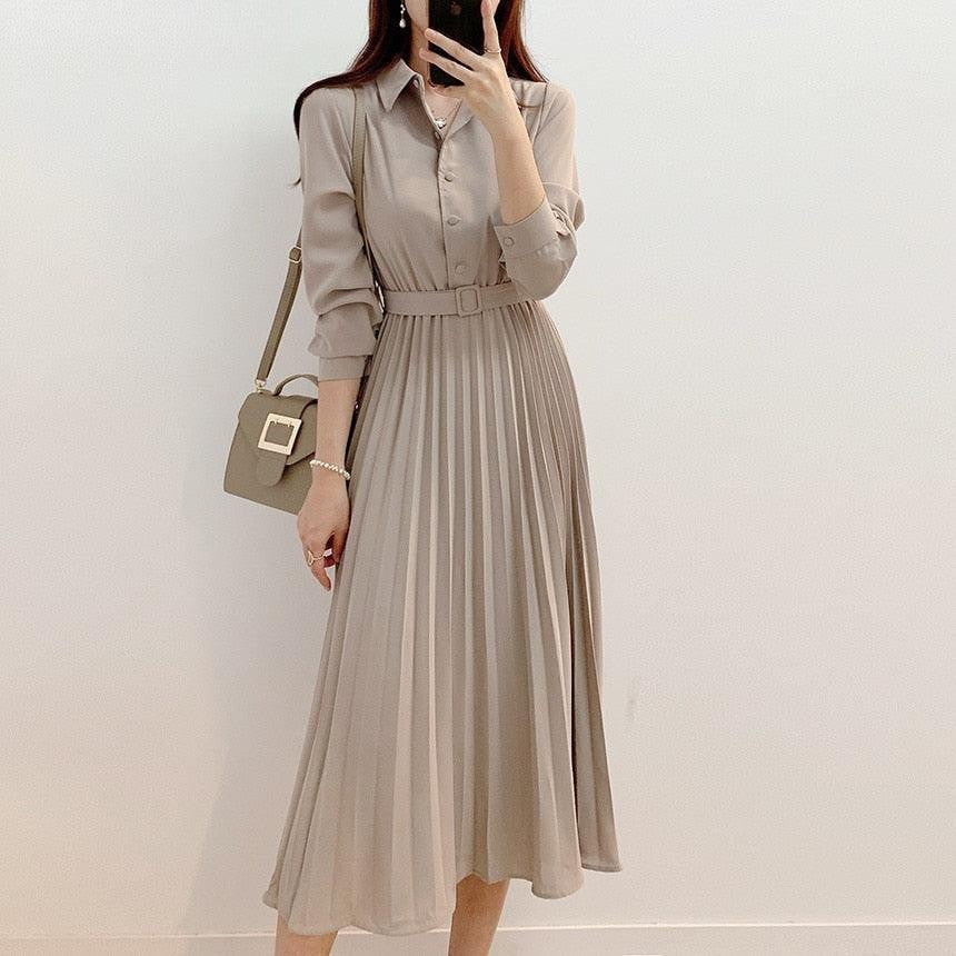 Woman wearing an apricot pleated midi shirt dress with a belt and matching handbag