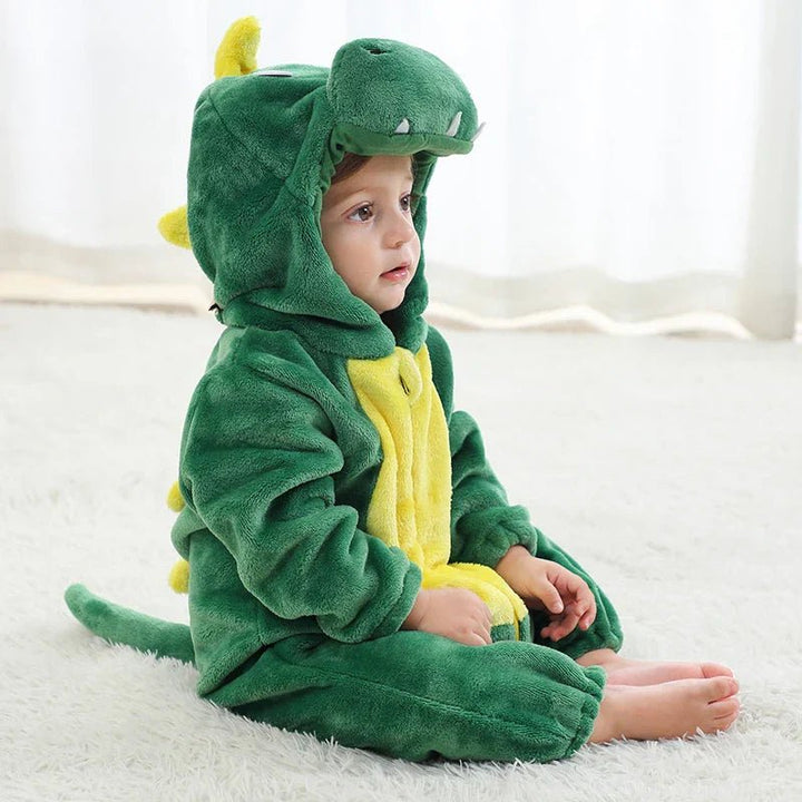 Cute baby sitting on a white rug wearing a green dinosaur animal onesie with a spiky tail and hood