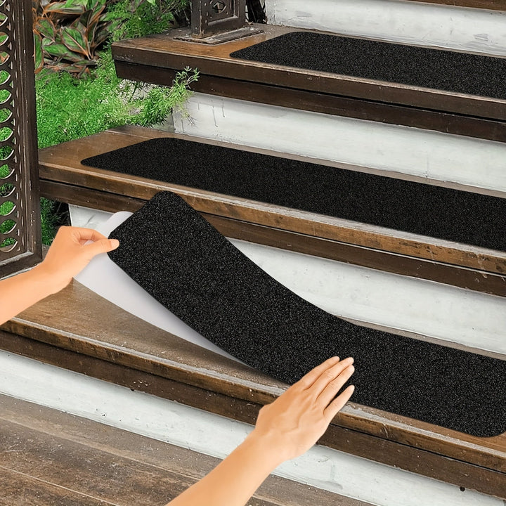 Person peeling backing off a black anti-slip stair tread on wooden steps