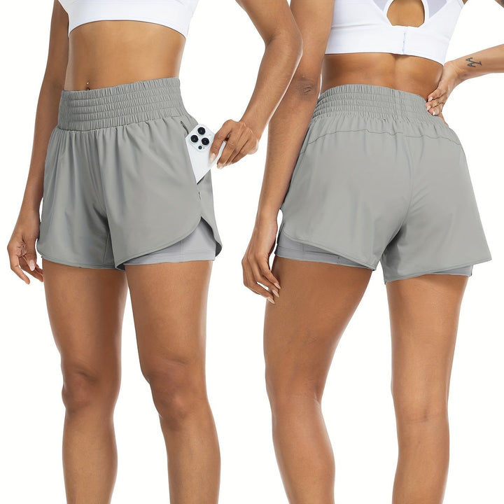 Model wearing light gray high-waisted double-layer athletic shorts with a phone in the side pocket, front and back view.