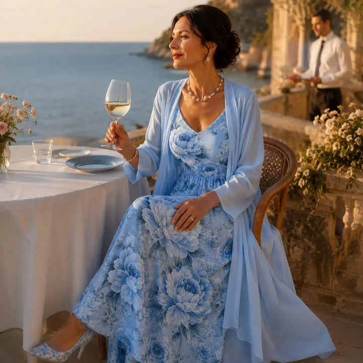 Woman sitting at a seaside table wearing a light blue floral maxi dress and duster set.