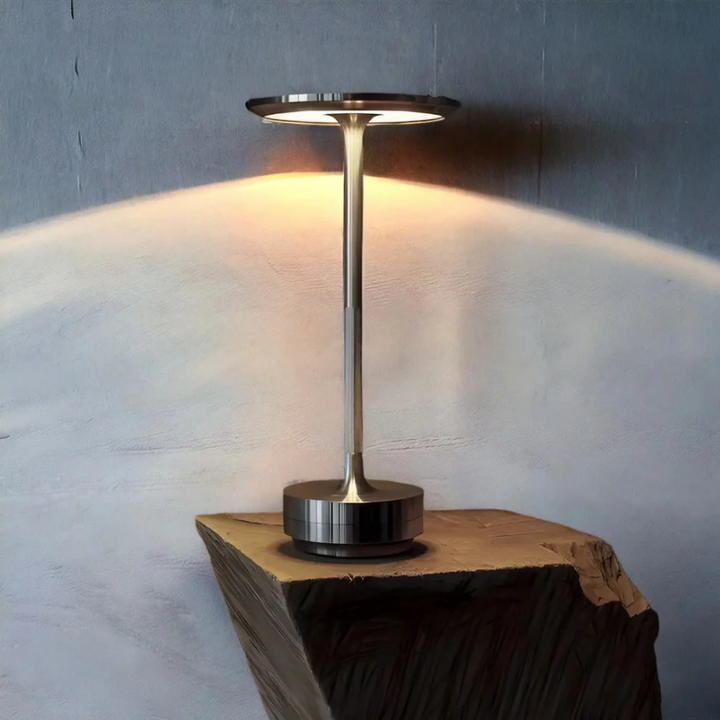 Grey wireless table lamp emitting warm ambient light on a rustic wooden stand.