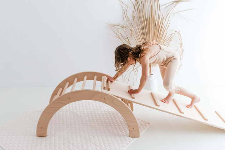 Child safely climbing wooden frame and rocker indoors, promoting active play and motor skills.