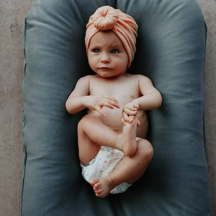 Baby wearing a cute peach headband resting in a grey baby lounger