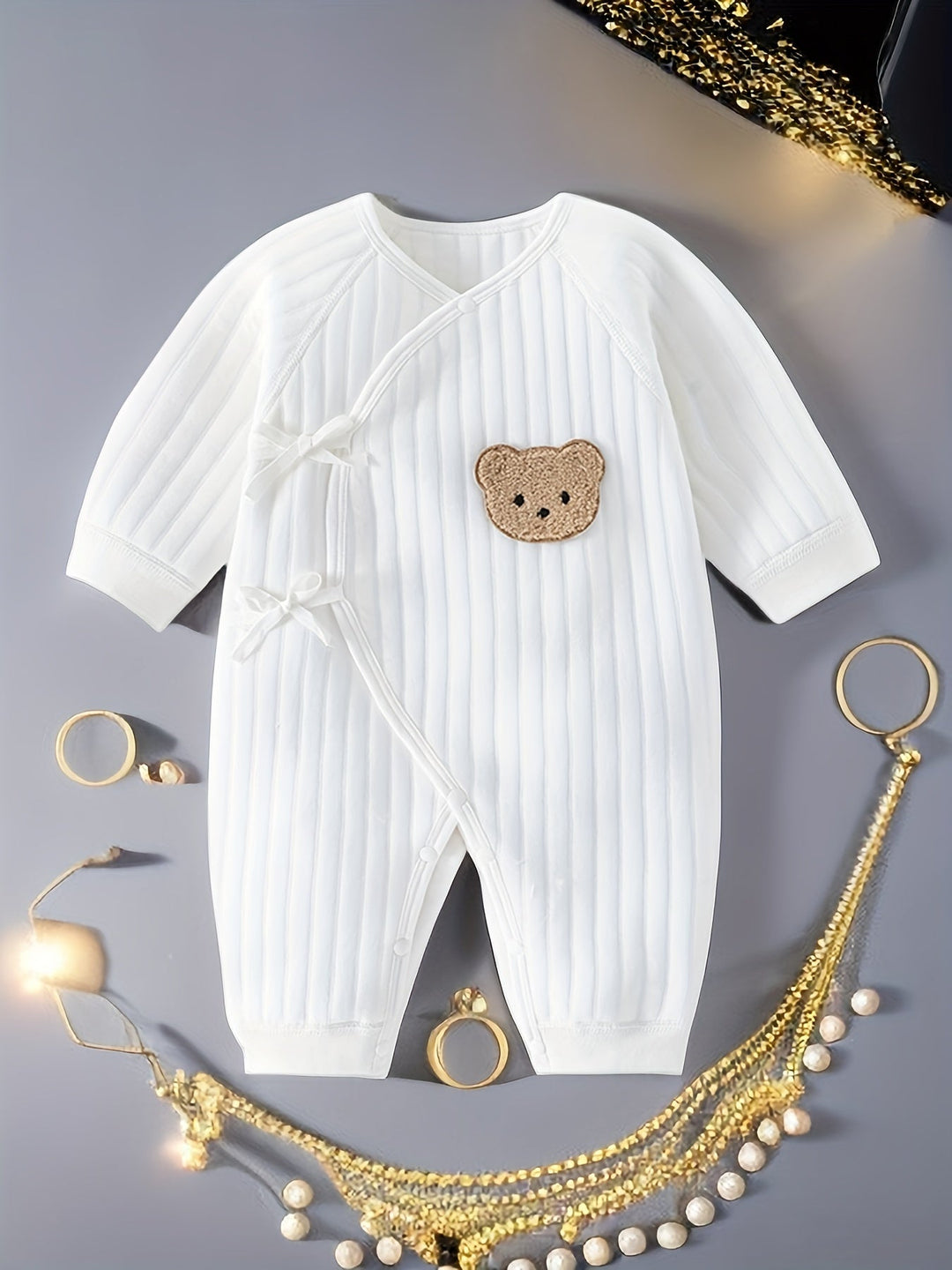 White baby romper with bear patch laid flat with decorative gold accessories