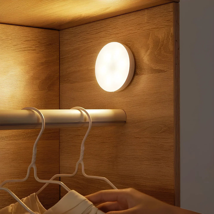Wireless motion sensor light mounted inside a wooden wardrobe next to clothing hangers