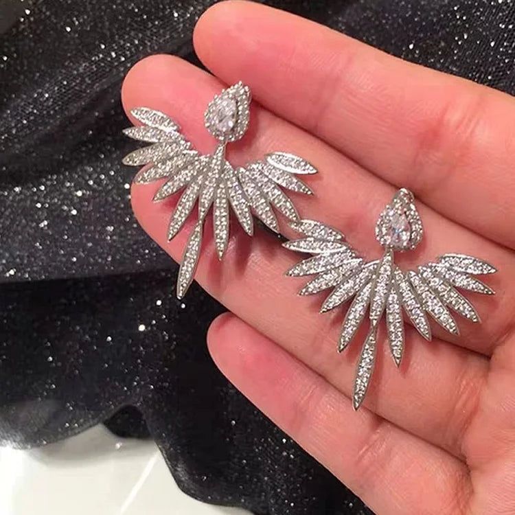 Close-up of sparkling angel wing silver stud earrings held in hand