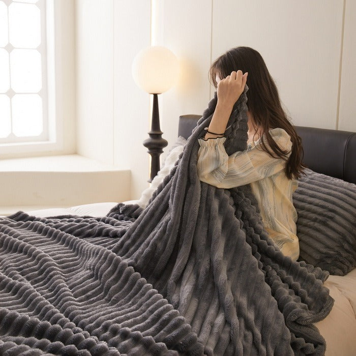 Person holding a dark grey ribbed throw blanket on a cozy bed setup