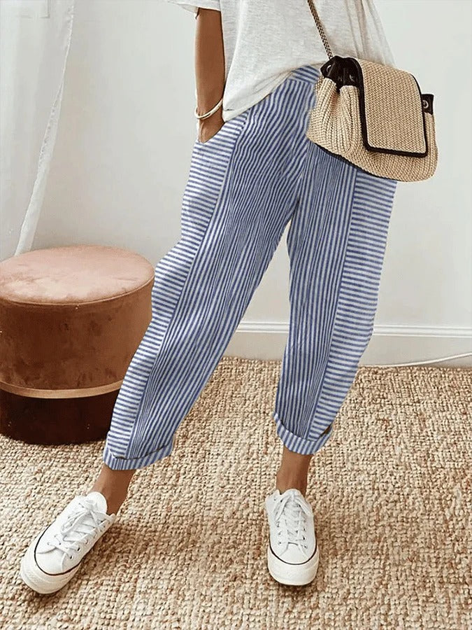 Woman wearing blue striped relaxed trousers with white sneakers and a crossbody bag