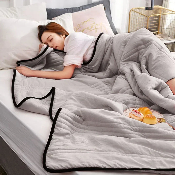 A woman sleeping comfortably under a grey breathable summer cooling blanket