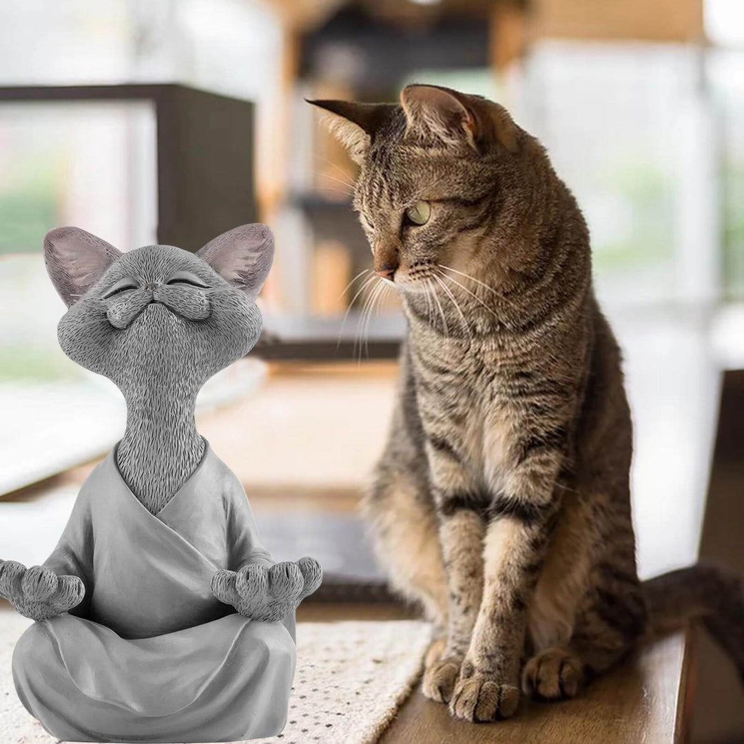 Grey meditating Buddha cat figurine sitting next to a real cat indoors