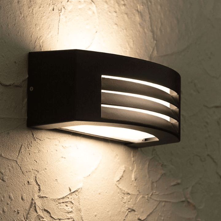 Close-up of modern black outdoor wall lamp emitting warm light on textured wall