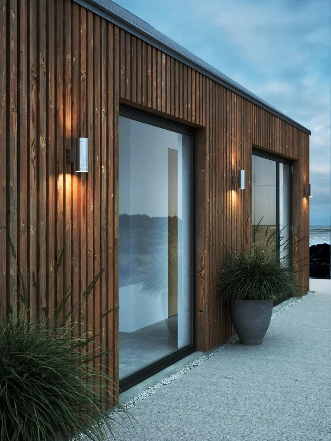 Exterior view of modern home illuminated by stylish up-down wall lamps at dusk