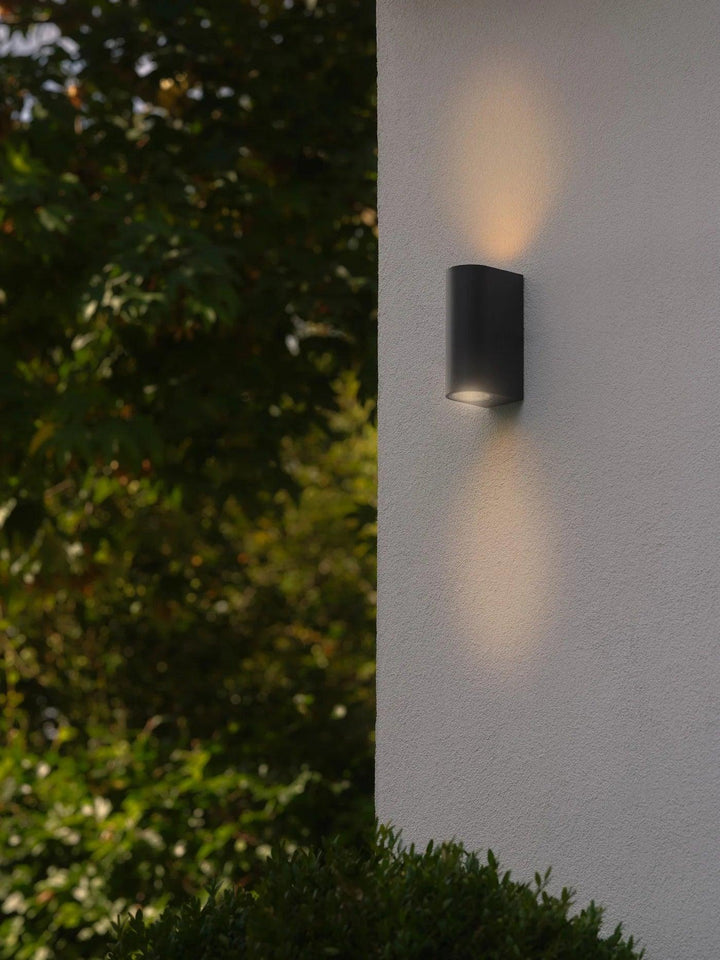 Modern black architectural facade wall lighting mounted next to garden foliage