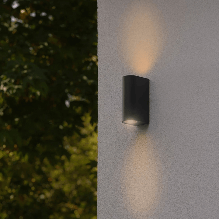 Dion black outdoor up-down wall light illuminating a white exterior wall at night