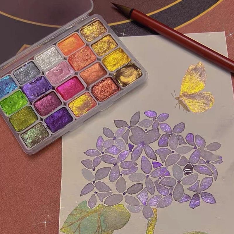 Multicolour watercolour paint palette next to a painted floral artwork and brush