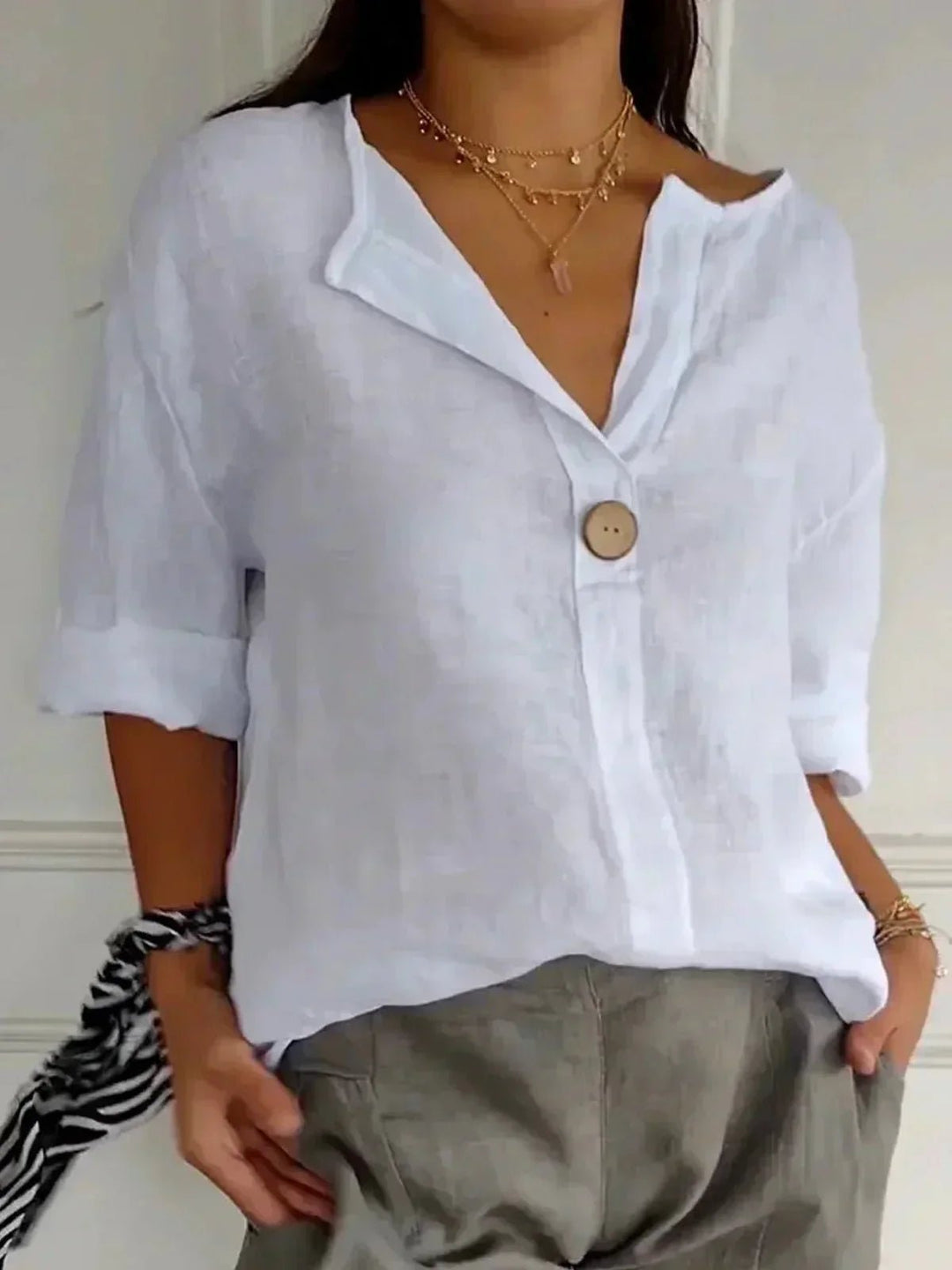 Woman wearing a white relaxed V-neck top with button detail and layered gold necklaces.