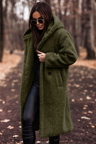 Woman wearing an olive green hooded winter coat in a wooded park setting