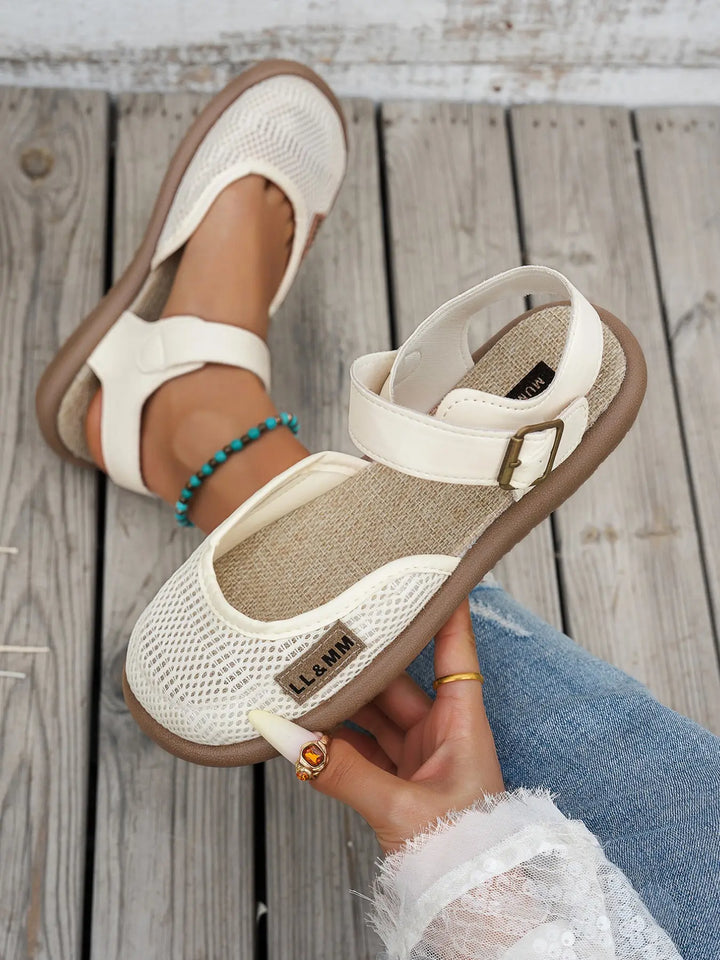 Close-up of cream women's closed-toe flat sandal held in hand
