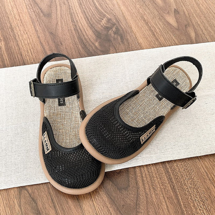 Pair of black closed-toe flat sandals displayed on textured mat