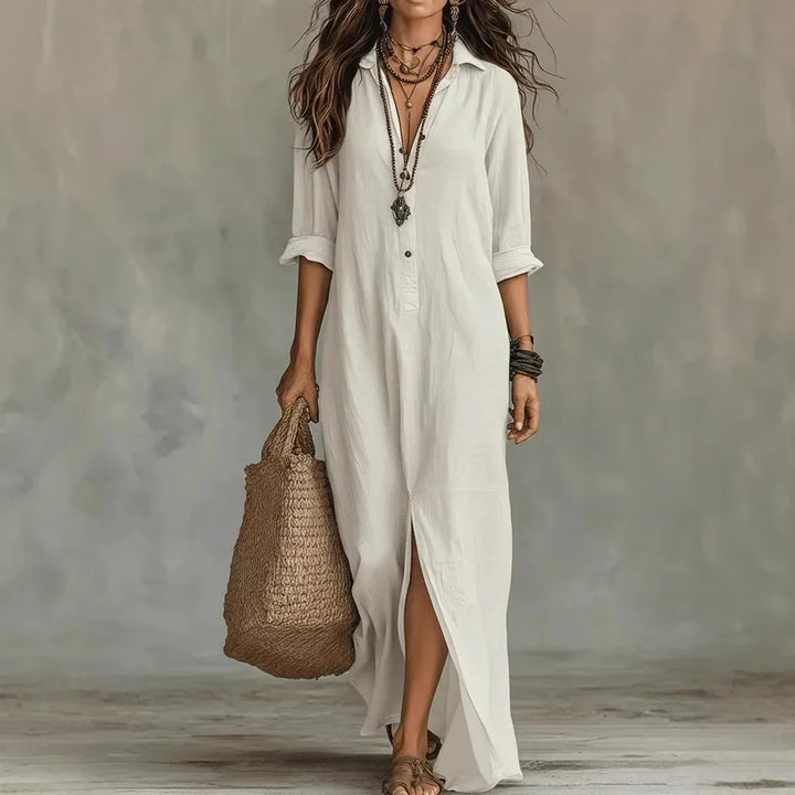 Woman wearing a long white button-front shirt dress with layered necklaces and a straw bag.