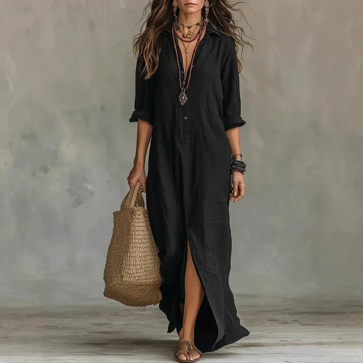 Woman wearing a long black button-front shirt dress with layered necklaces and a straw bag.