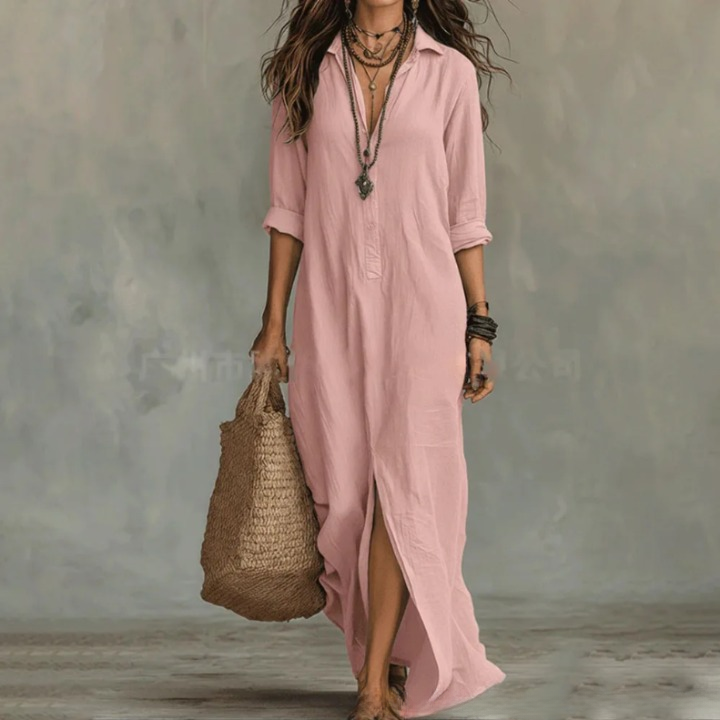 Woman wearing a long pink button-front shirt dress with layered necklaces and a straw bag.