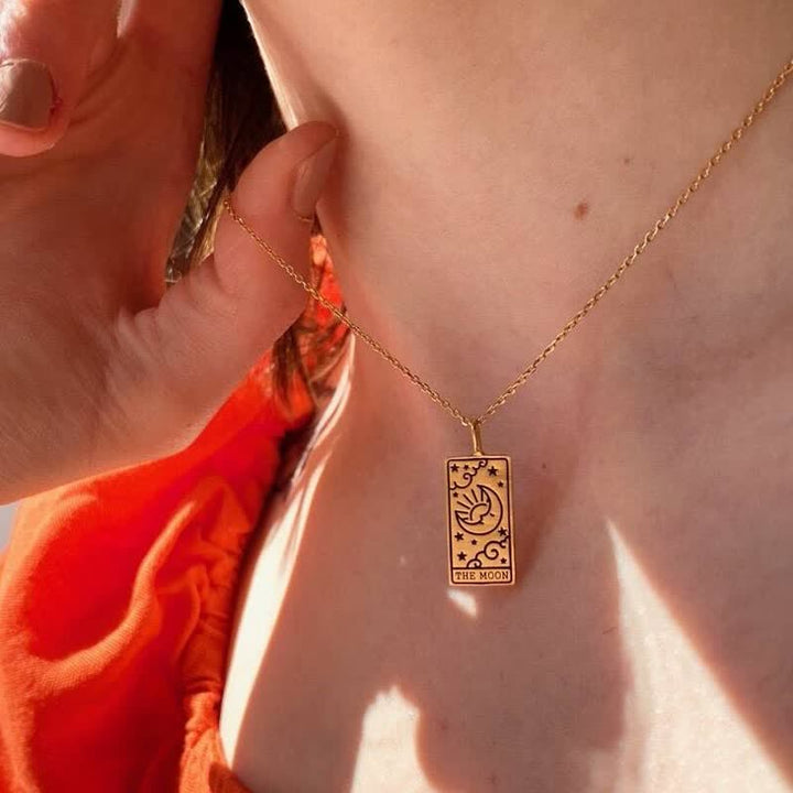 Woman wearing the Moon tarot card pendant necklace in gold paired with an orange top.