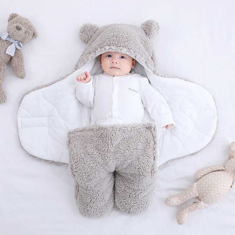 Baby wrapped in a grey bear ear sleeping bag lying on a white bed