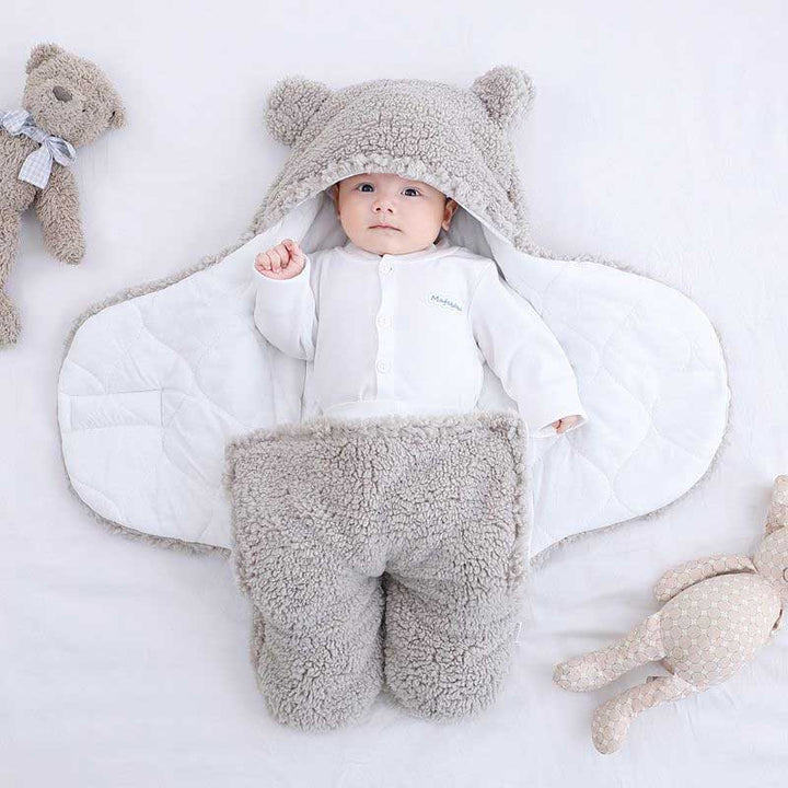 Baby wrapped in a grey bear ear sleeping bag lying on a white bed