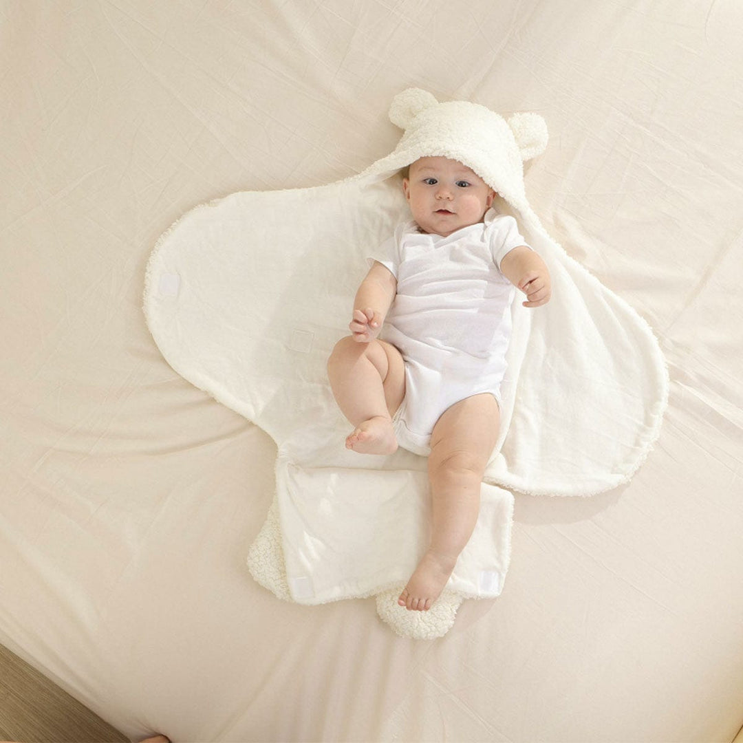 Baby lying on an open white bear ear swaddle wrap blanket