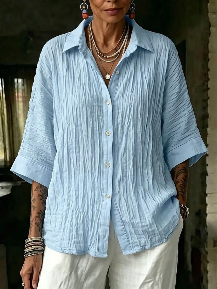 Front view of a woman wearing a light blue crinkle texture button-down shirt with 3/4 sleeves.