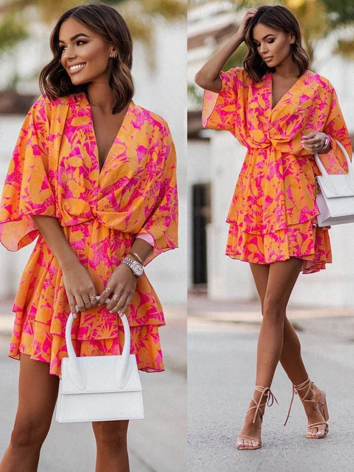 Model wearing a vibrant orange and pink floral mini dress with a white handbag