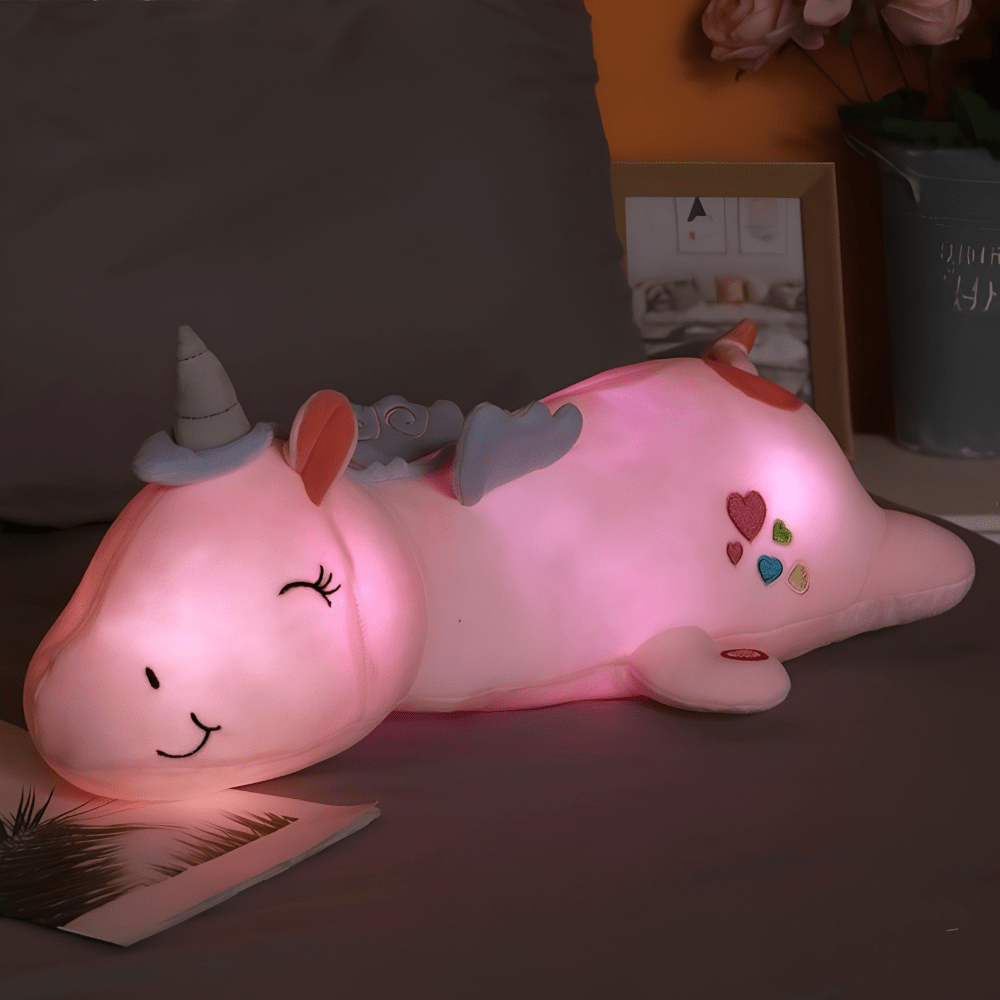 Pink plush unicorn night light glowing softly on a bed
