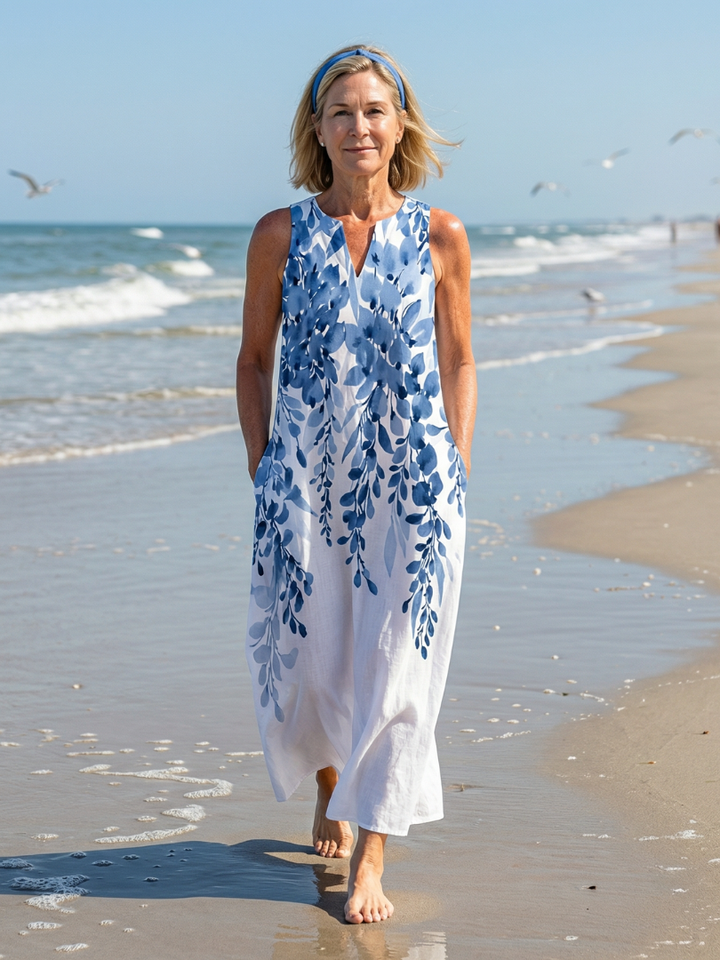 Woman walking on a beach wearing a white sleeveless floral maxi summer dress