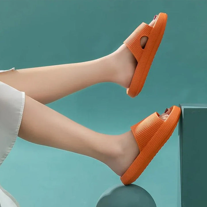 Person wearing vibrant orange cloud recovery slides against a teal background
