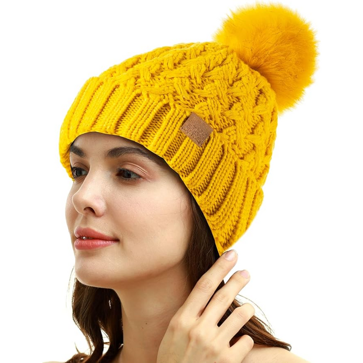 Woman wearing a bright yellow winter pom beanie with textured cable knit