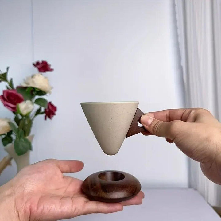 A hand holding a conical coffee cup above its matching dome wooden coaster
